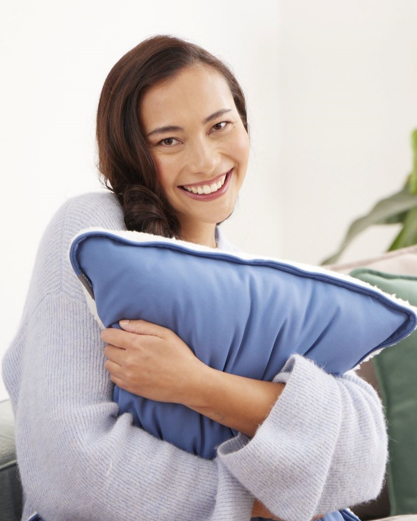 Woman hugging a blue medisana heated pad and enjoying soothing warmth.